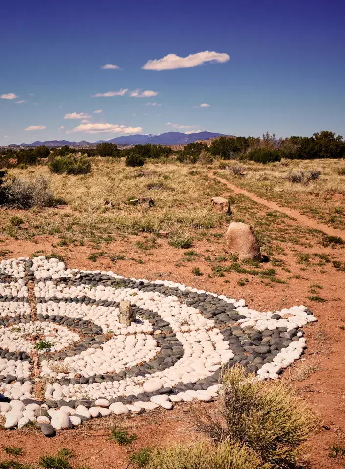 A spiral stone labyrinth sits in a grassy landscape with distant mountains under a clear blue sky.
