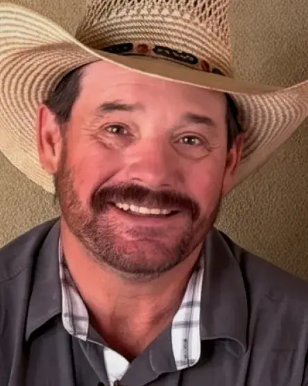Smiling man in a straw cowboy hat and gray shirt, showcasing a friendly demeanor against a neutral background.