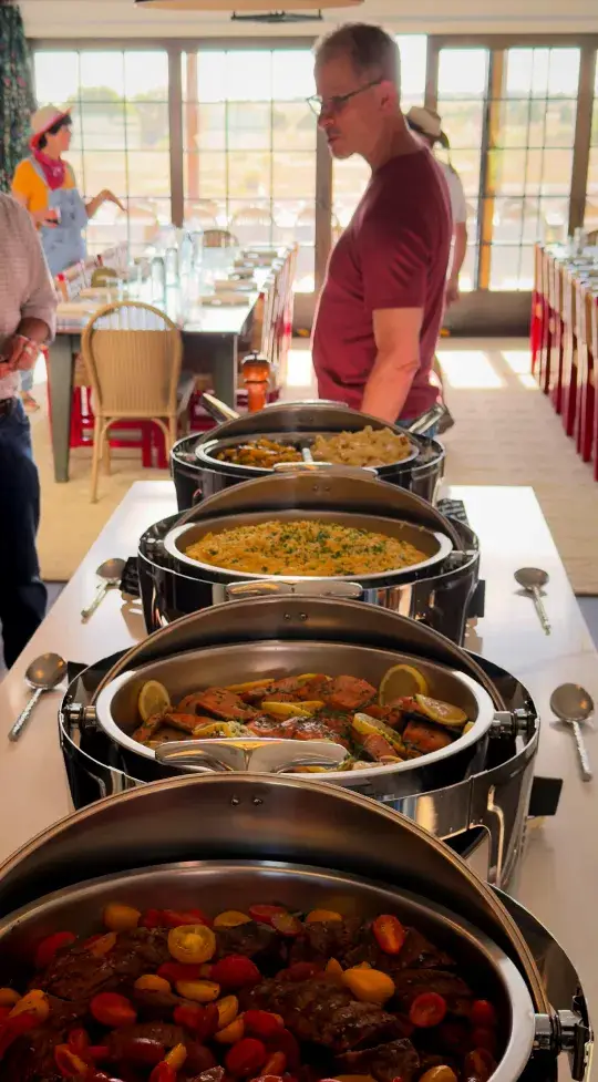 A buffet featuring various dishes with a man selecting food, set in a bright dining area with a long table.