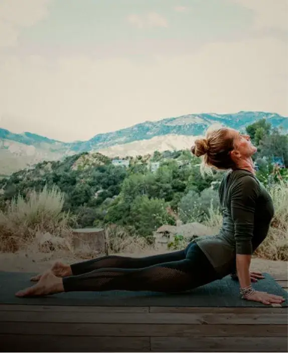A woman practices yoga in a serene outdoor setting, stretching in the cobra pose with mountains in the background.