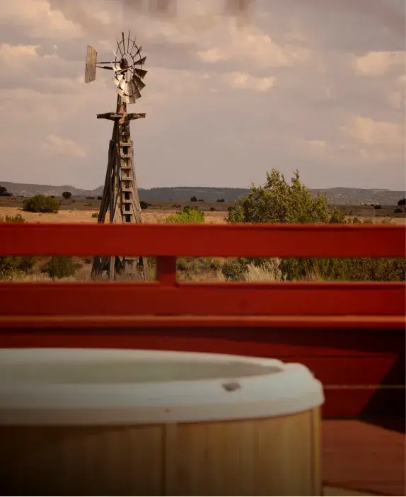 A rustic windmill stands in the distance, framed by a wooden railing and a hot tub in the foreground.