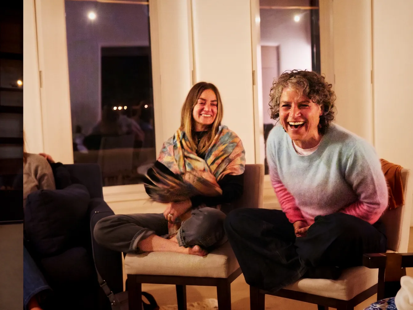 Two women laugh together in a cozy indoor setting, enjoying a warm and joyful moment.