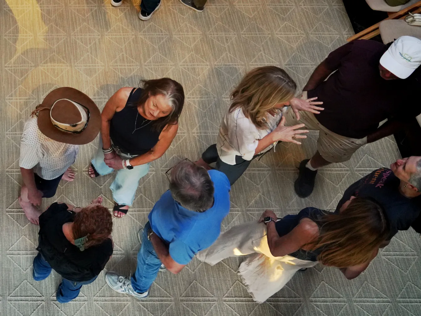 A group of people engaged in conversation in a spacious indoor setting with a patterned floor.
