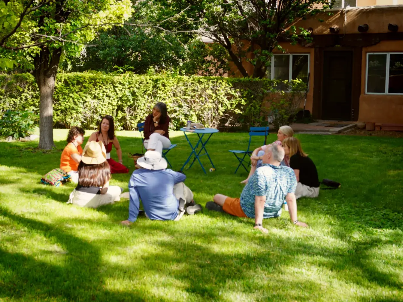 A group of people engaged in discussion outdoors at a Leadership Retreat Venue, surrounded by greenery and sunshine.