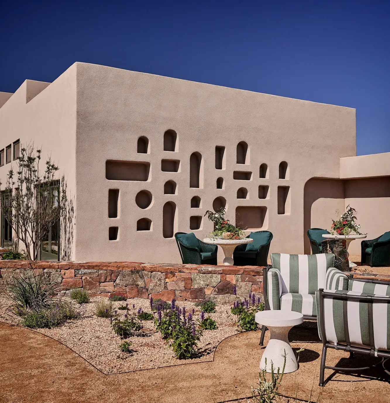 Modern adobe-style architecture features unique cutouts, surrounded by landscaped seating areas and desert plants.
