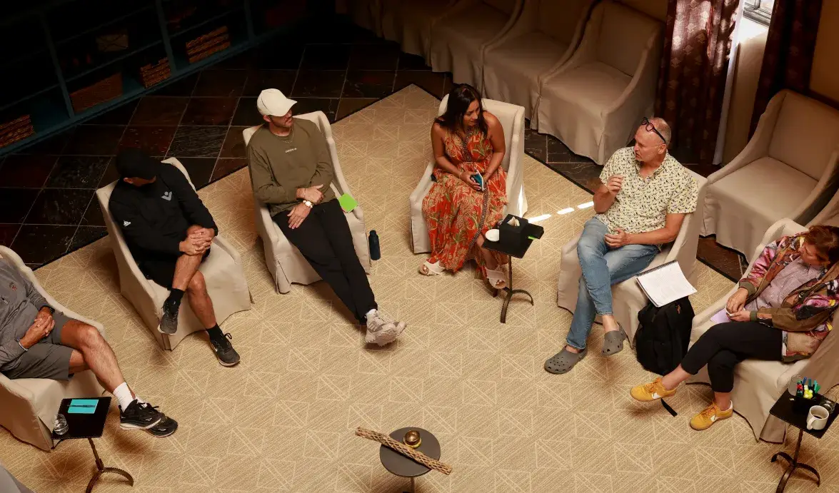 A diverse group of six individuals engaged in a discussion in a cozy, well-lit setting with chairs arranged in a circle.