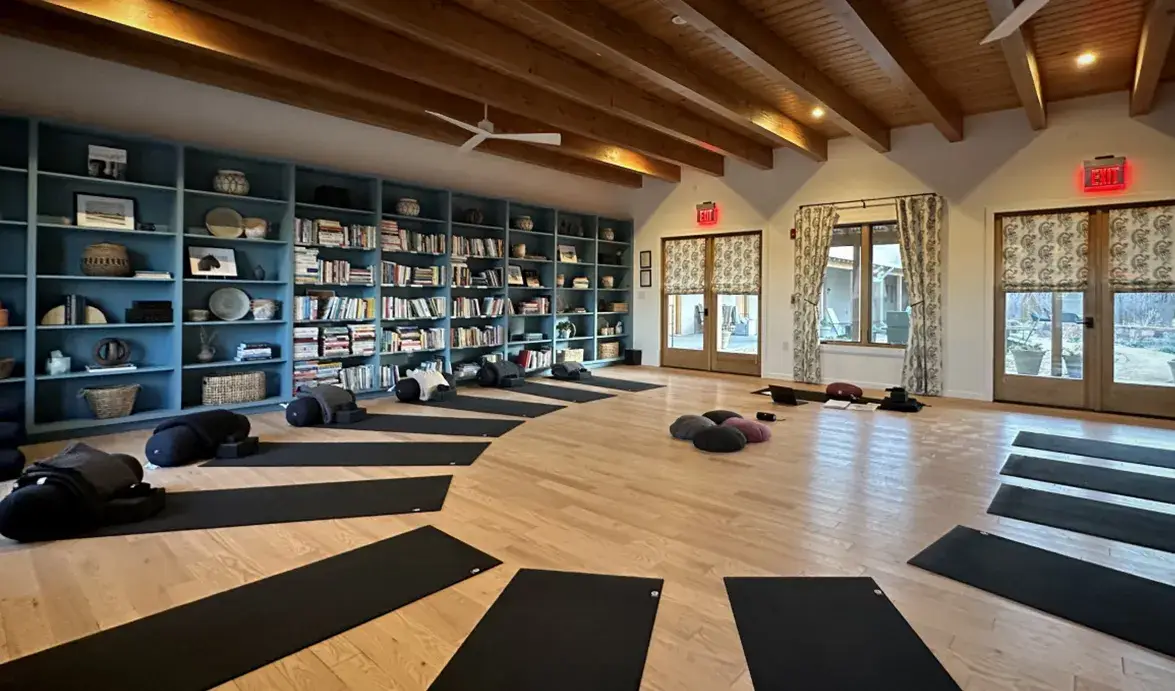 Spacious yoga studio with mats arranged in a circular pattern, surrounded by bookshelves and natural light.