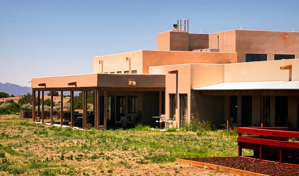 Modern adobe-style home with a spacious patio and surrounding natural landscape under a clear blue sky.