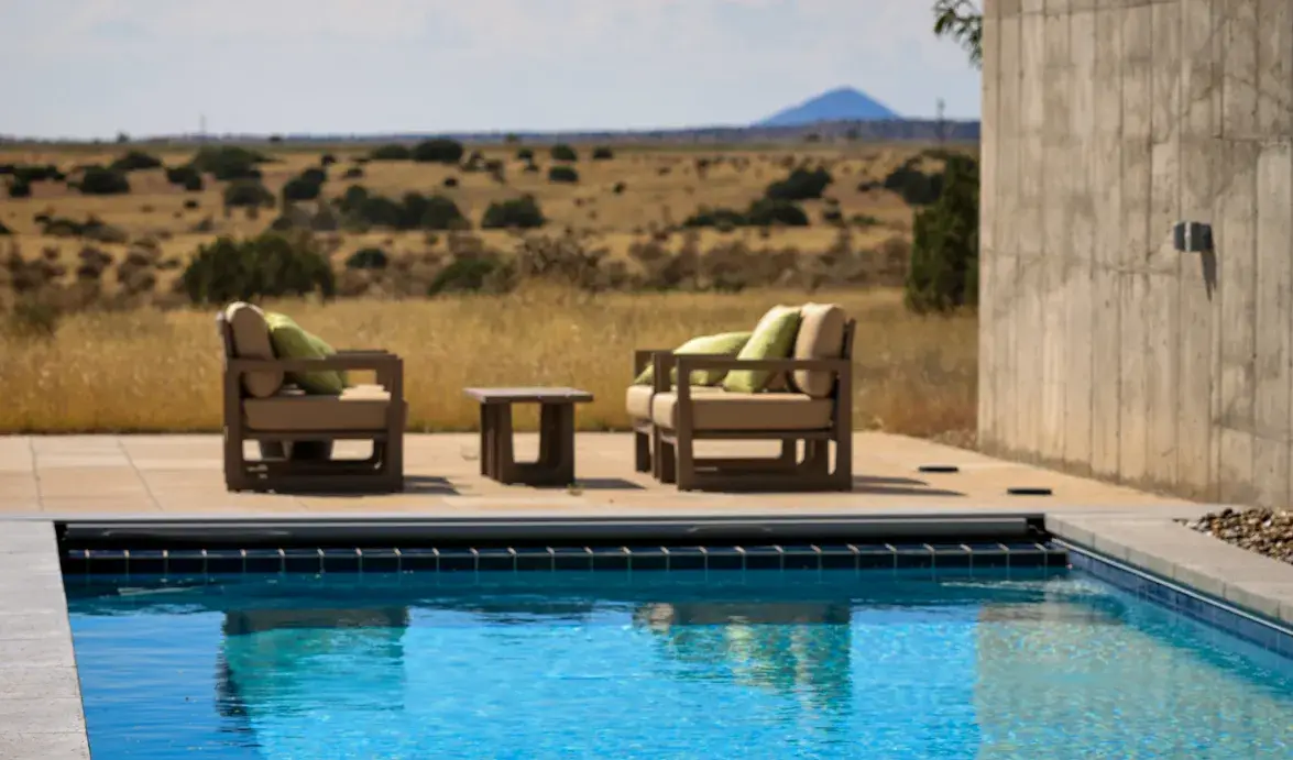 A serene outdoor space features a swimming pool, two chairs with green cushions, and a distant mountain view.