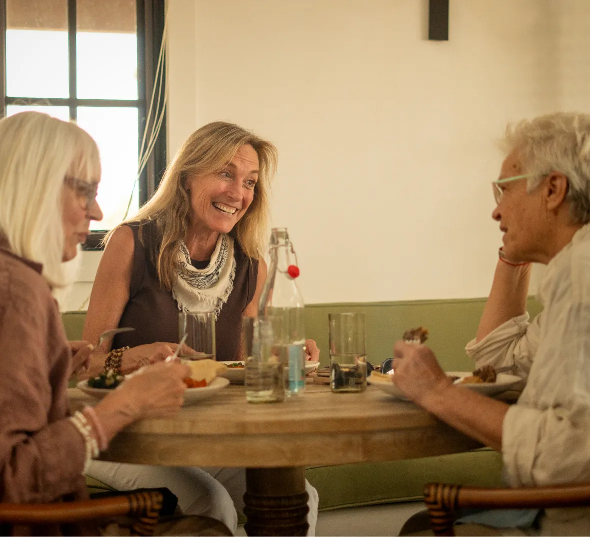 Three friends enjoy a lively meal together, sharing smiles and conversation at a cozy dining table.