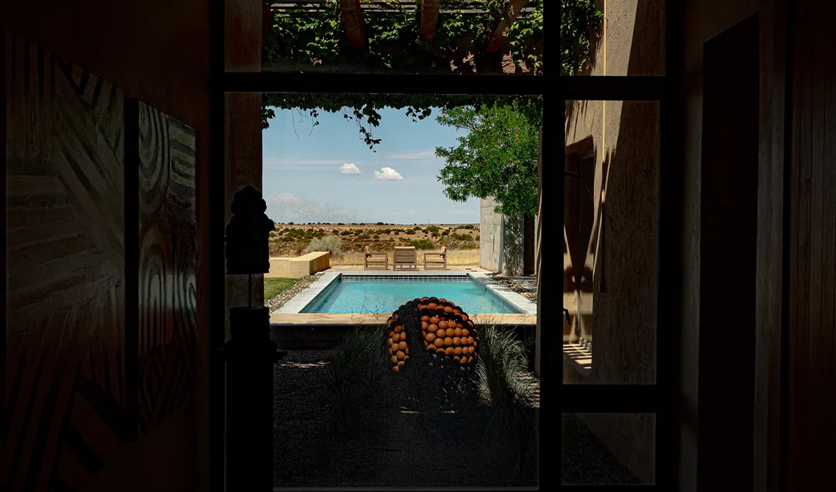 A serene view of a pool surrounded by desert landscape, framed by an indoor entrance with decorative elements.