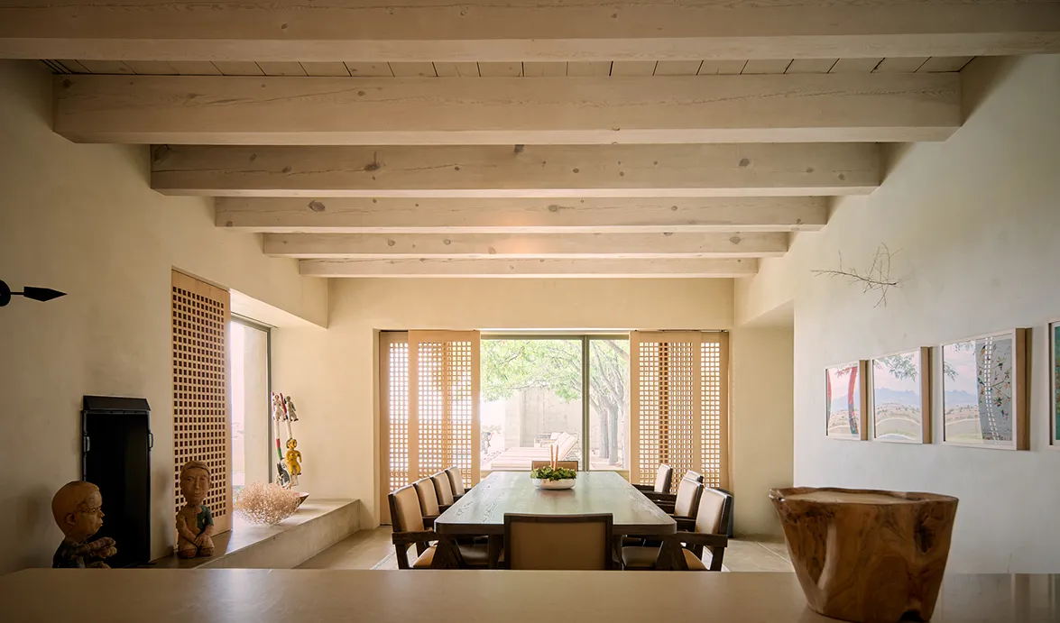 Spacious dining area with wooden beams, a long table, and natural light from large windows, featuring decorative elements.
